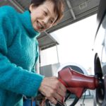 An older Asian woman fills up her car with petrol at the service station.