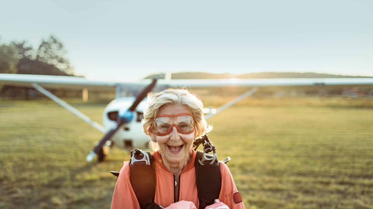 An older woman with a huge smile on her face having just touched down on the ground from skydiving.