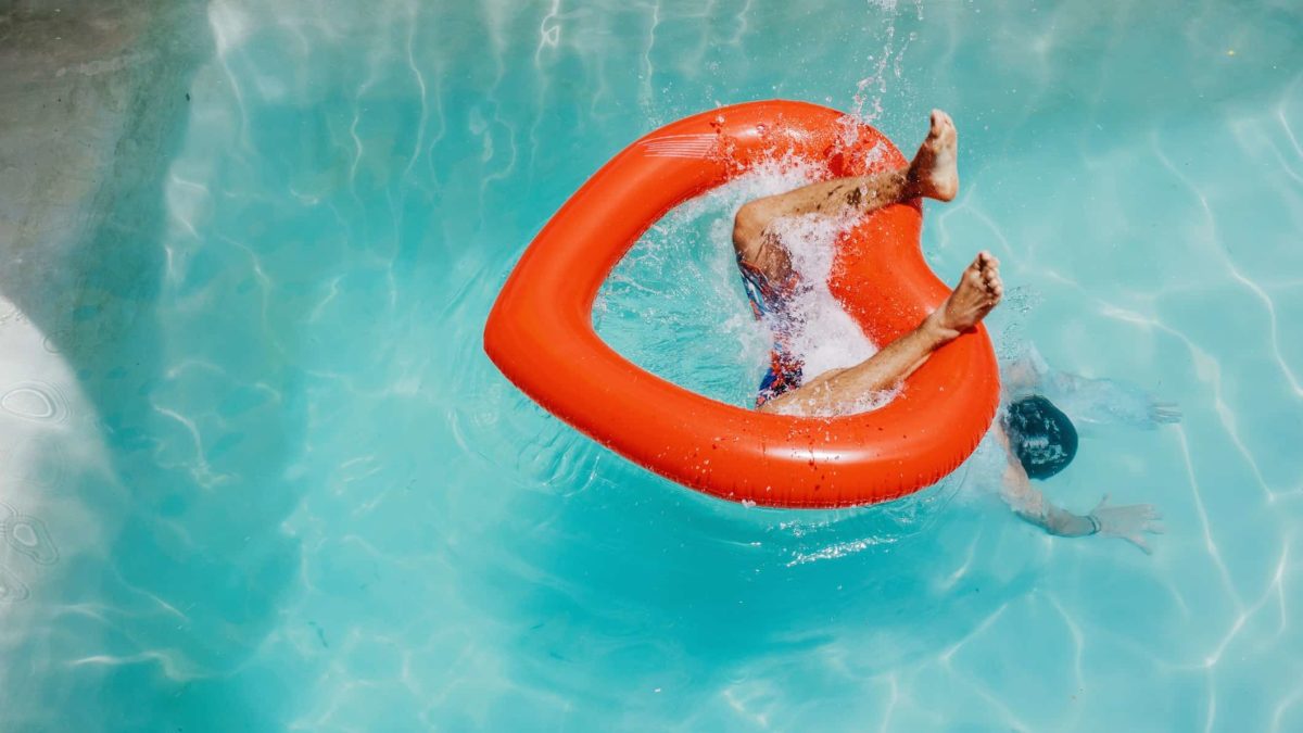 A person plunges into the pool with only their feet visible above the surface, diving through a heart-shaped inflatable ring.