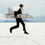 A man in a cardboard rocket ship and helmet zooms across the salt flats.