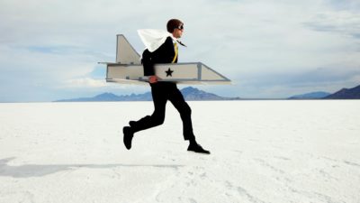 A man in a cardboard rocket ship and helmet zooms across the salt flats.