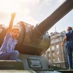 Two boys play outside on an old army tank.