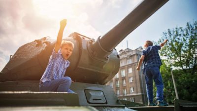 Two boys play outside on an old army tank.