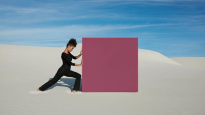 A woman pushing a large purple square along a beach.