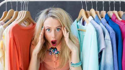 A woman peers through a bunch of recycled clothes on hangers and looks amazed.