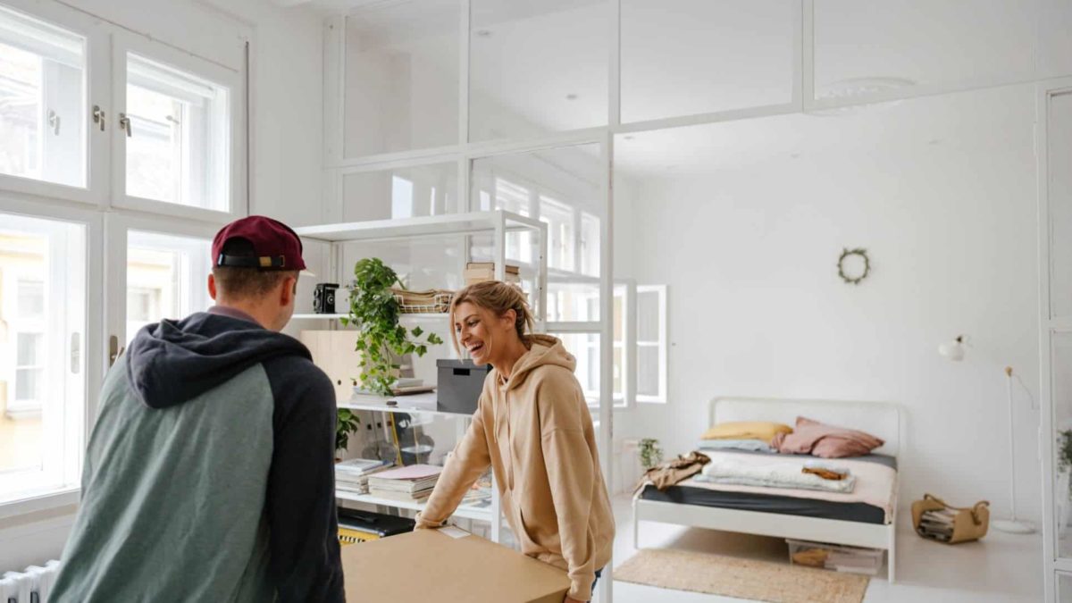 A happy man and woman holding a small dining table moving into their apartment