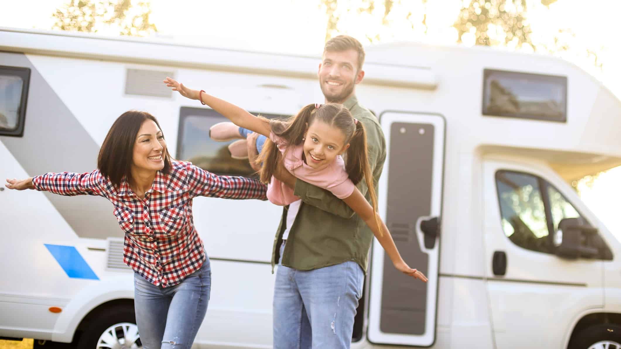 Man holds young girl out in a flying motion as mum watches on, all in front of a motorhome.
