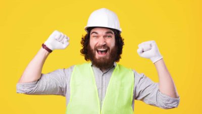 Happy man in high vis vest and hard hat holds his arms up with fists clenched celebrating the rising Fortescue share price