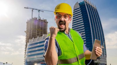 Construction worker in hard hat pumps fist in front of high-rise buildings