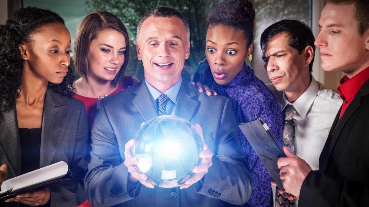 One businessman holds crystal ball while him and five others gather round to look into the future