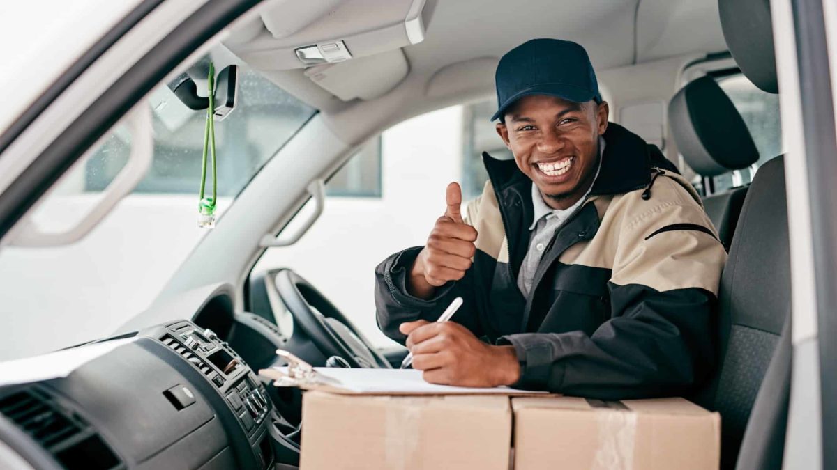 A delivery driver leans on boxes in his van as he puts his thumb up.