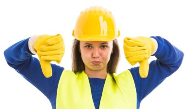 Woman in yellow hard hat and gloves puts both thumbs down