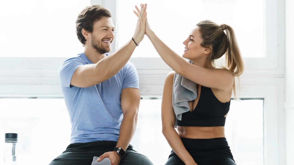 A man and woman high five each while sitting down after working out at the gym.