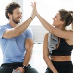 A man and woman high five each while sitting down after working out at the gym.