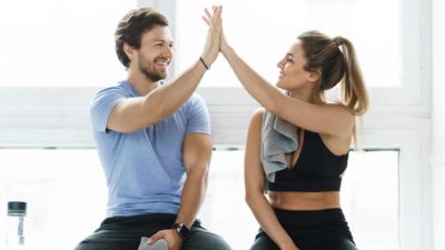 A man and woman high five each while sitting down after working out at the gym.