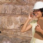 A mining executive from Red Dirt Metals chats on her mobile phone looking pleased with a mining site and mining truck in the background