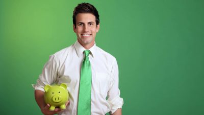 Young man in white shirt and green tie with green background holding green piggy bank