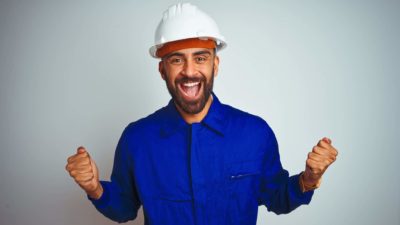 A mining employee in a white hard hat cheers with fists pumped as the Hot Chili share price rises higher today