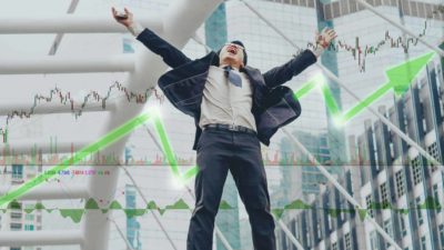 Man jumps for joy in front of a background of a rising stocks graphic.