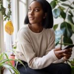 A woman looking through a window with an iPhone in her hand.
