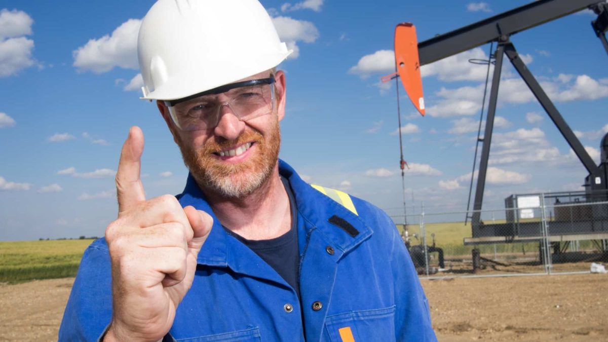 A man in a hard hat puts his finger up to say 'number one' in front of an oil mine