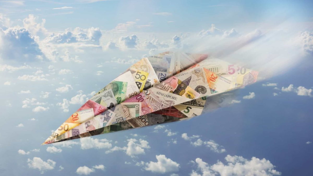 Paper plane made of money in different currencies flies through the sky