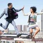 Two people jump and high five above a city skyline.