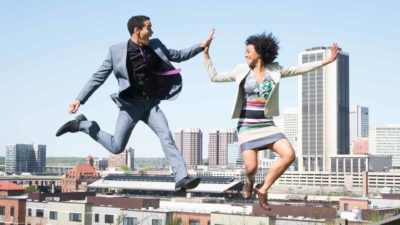 Two people jump and high five above a city skyline.