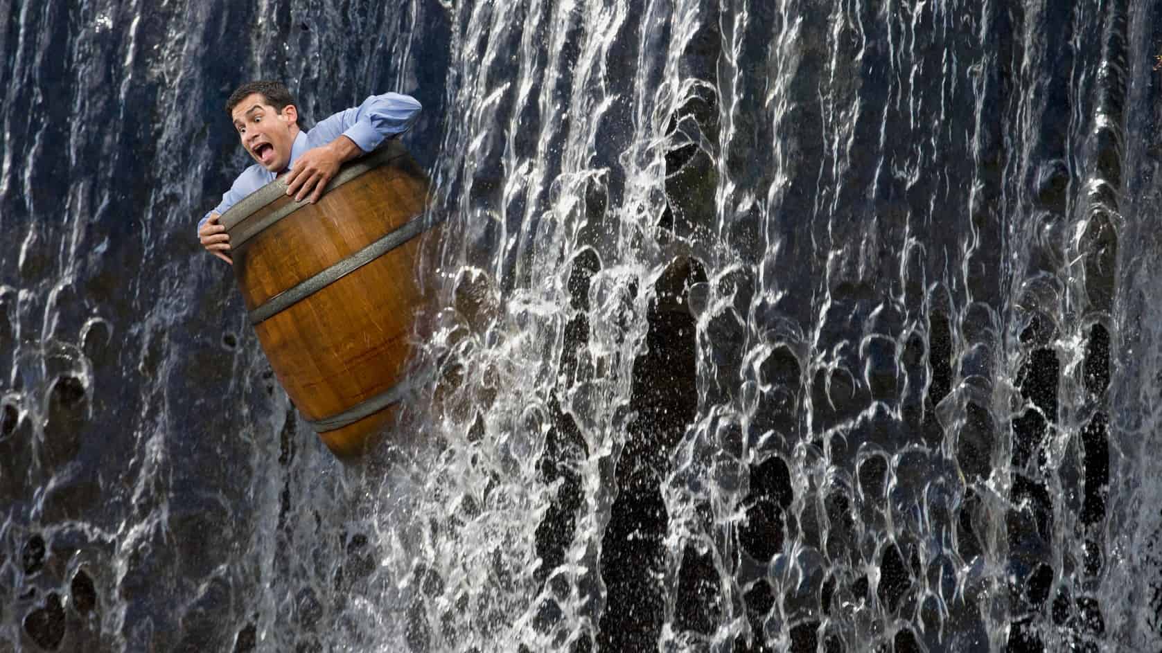 Businessman in a barrel plunges down a waterfall