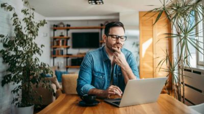 A man sitting at his dining table looks at his laptop and ponders the CSL balance sheet and the value of CSL shares today