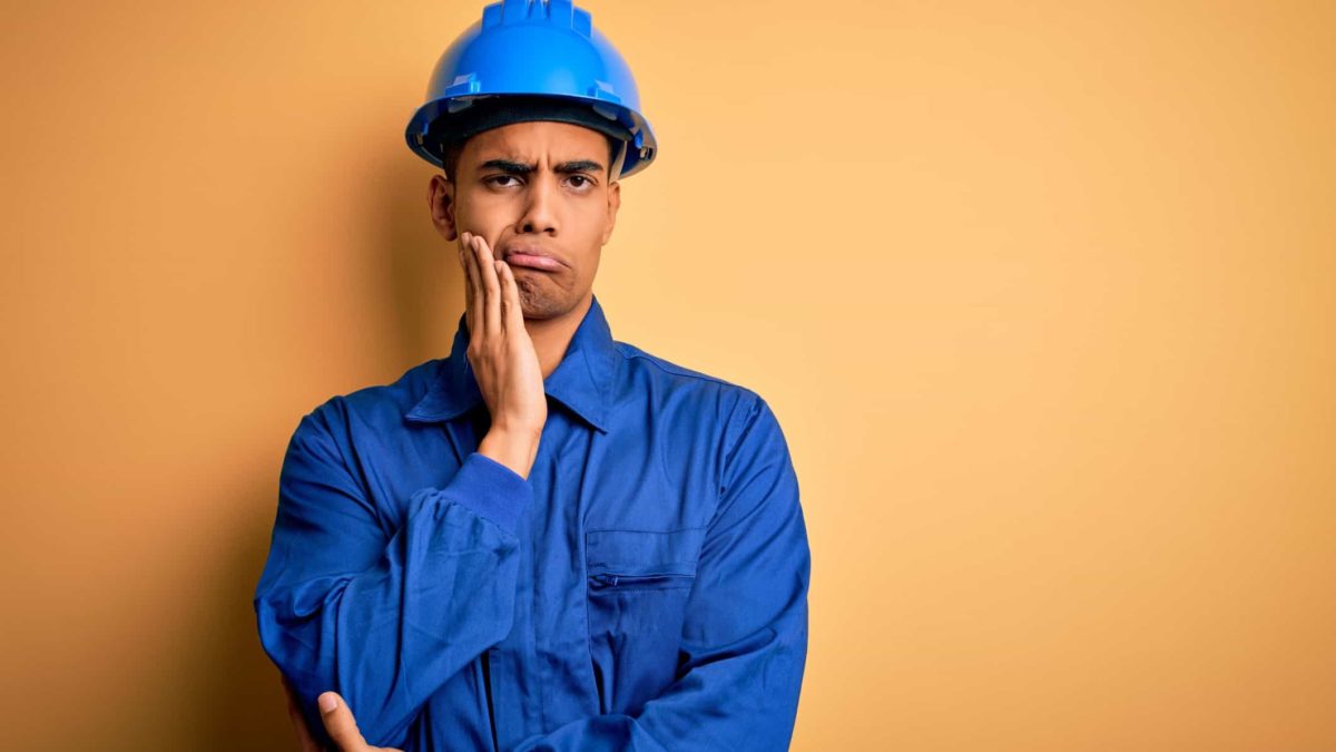 Worker in hard hat looks puzzled with one hand on chin
