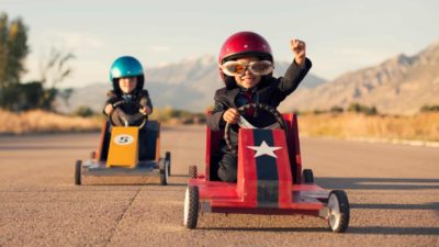 Young boy in business suit punches the air as he finishes ahead of another boy in a box car race.