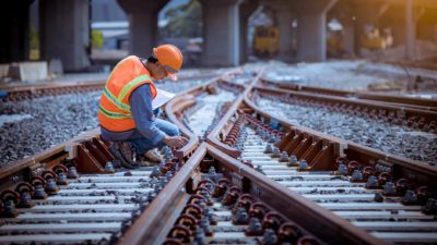 Rail worker in hard hat kneels over train tracks inspecting tracks