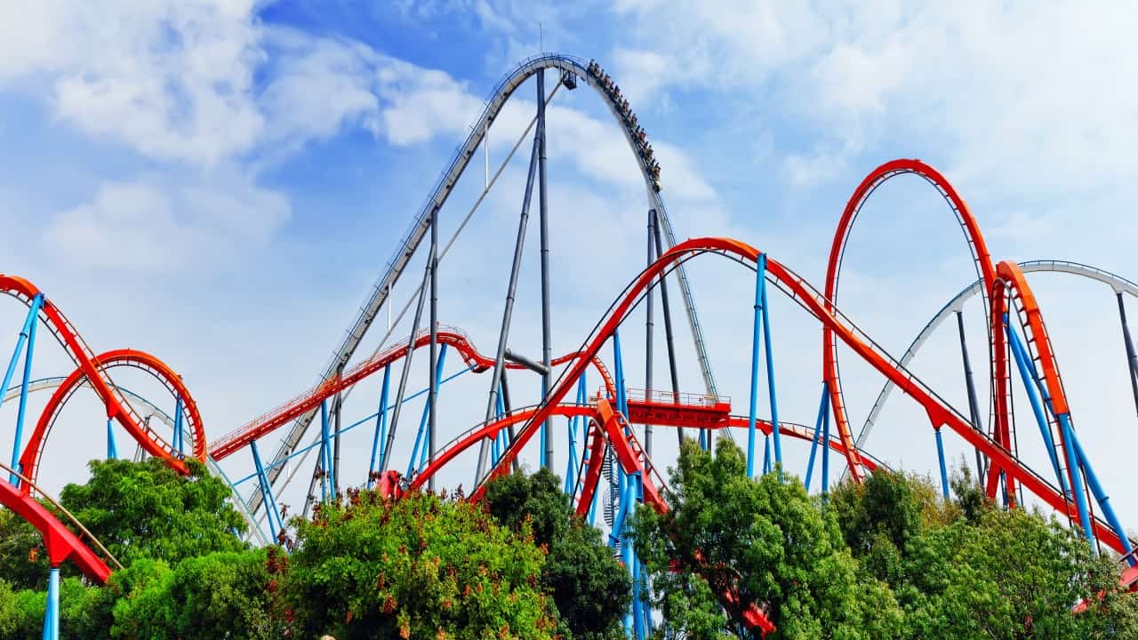 A big red and blue rollercoaster circuit photographed from far away with the blue sky in the background