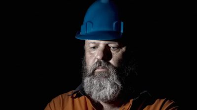 Miner with blue hard hay looks downward and looks upset