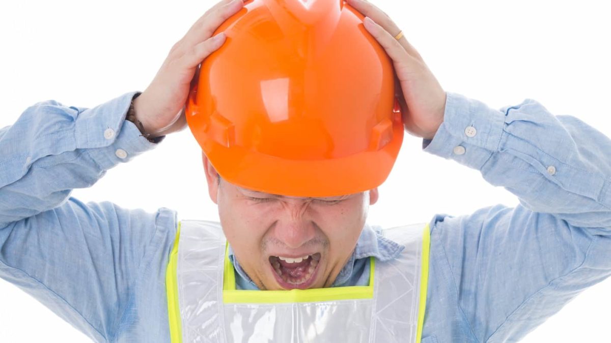 A miner wearing a high-vis vest and orange hardhat bows his head and puts his hands on his head and screams as the Hawsons Iron share price falls today despite a new progress report on its flagship project
