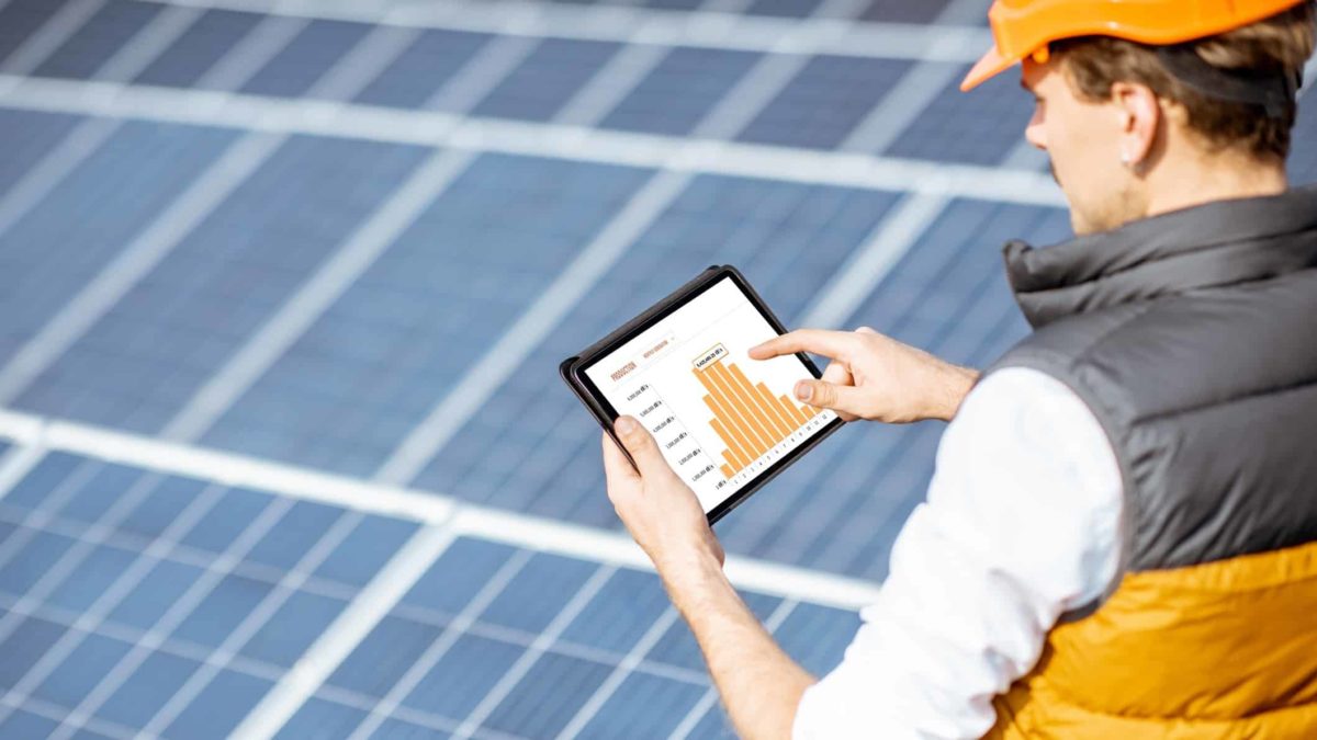 Builder looking at ipad standing in front of solar panels