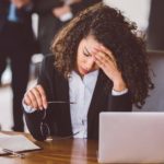 Stressed business woman sits at desk with head resting on her hand