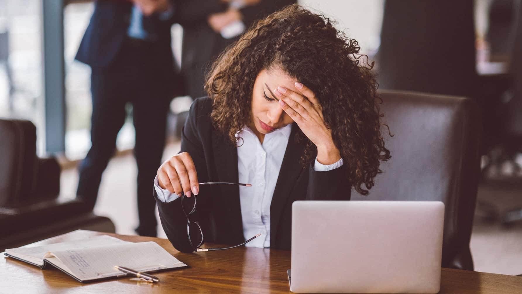 Stressed business woman sits at desk with head in hand.