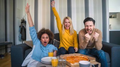Three people sit on safe cheering with pizza on table