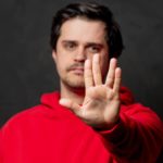 Man in red jumper holds hand out in a vulcan salute.