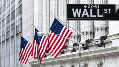 Three United States flags and a Wall St sign outside the US financial building.