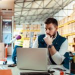 An industrial warehouse manager sits at a desk in a warehouse looking at his computer while the Centuria Industrial share price rises