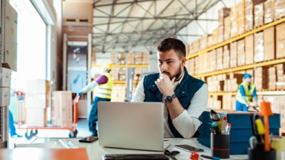 An industrial warehouse manager sits at a desk in a warehouse looking at his computer while the Centuria Industrial share price rises