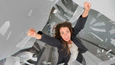 A woman puts her hands up as she smashes and breaks through a glass ceiling.