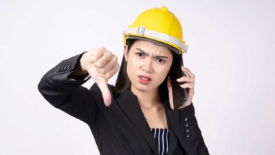 Female worker in hard hat puts thumb down while on the phone