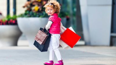 Young girl looks bag at camera as she walks in the street with several shopping bags.