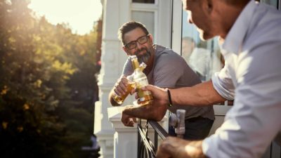 Two men standing on a balcony cheers their bottles.