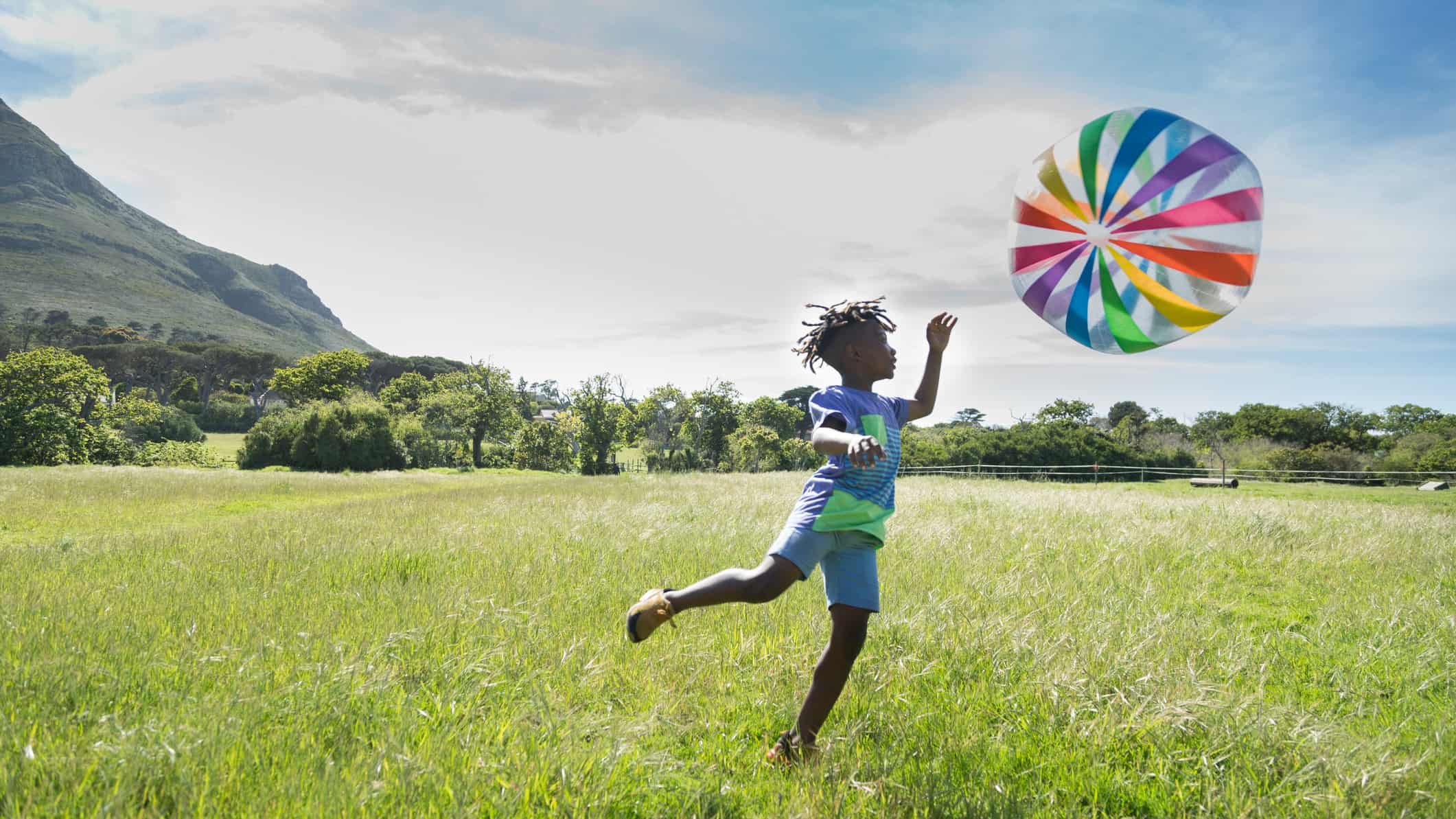 A boy bounds after a big colourful bouncing ball in a grassy field.