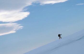 A sole trekker climbs a steep snowy mountain.